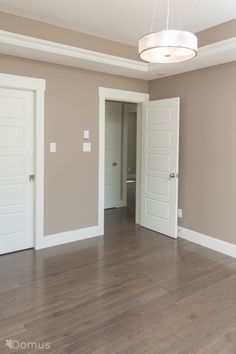 an empty living room with two doors and hard wood flooring on the other side