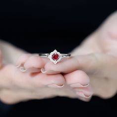 a woman's hands holding a ring with a red stone in it and the other hand