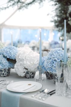 the table is set with blue and white hydrangeas, silverware, and candles