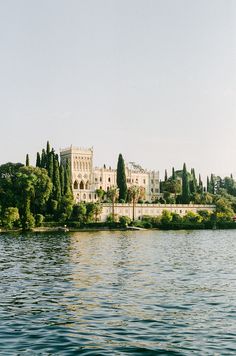 a large castle sitting on top of a lush green hillside next to a lake filled with water