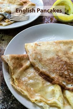 two white plates topped with pancakes on top of a wooden table next to lemon wedges