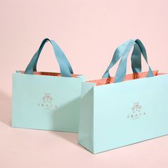 two blue shopping bags sitting side by side on a pink and green background with the handles down