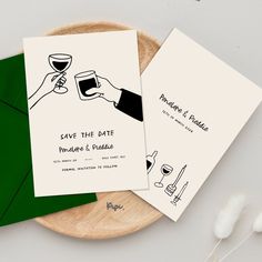 two wedding cards with wine glasses on them and green envelopes next to each other