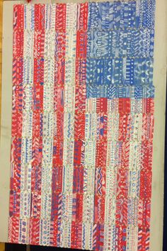 an american flag made out of strips of red, white and blue fabric on a piece of wood