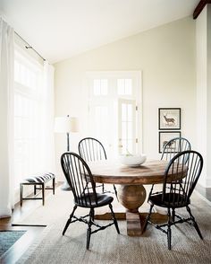 a dining room table with four chairs and a bowl on top of it in front of two windows