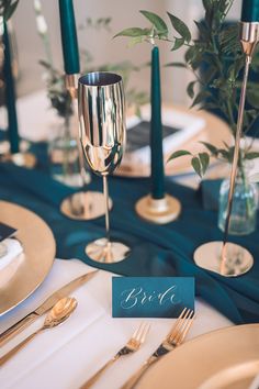 the table is set with gold and blue place settings, silverware, and greenery