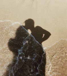 the shadow of a person standing on top of a rock next to a body of water