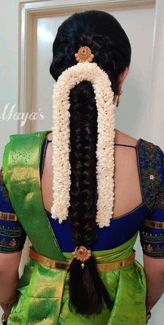 a woman wearing a green and blue saree with flowers in her hair is seen from the back