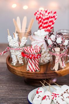 candy and marshmallows in glass jars on a wooden tray with red and white striped lollipop sticks