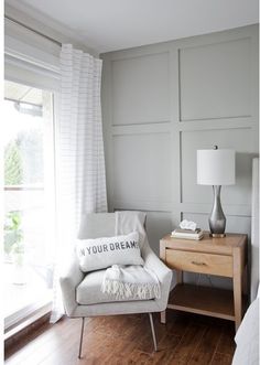 a white chair sitting in front of a window next to a table with a lamp on it