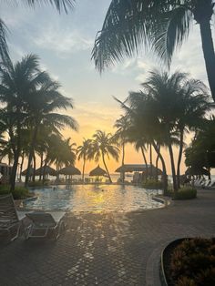 an empty swimming pool surrounded by palm trees with the sun going down in the distance