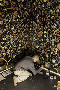 a man sitting on the floor in front of a wall covered with flowers and leaves