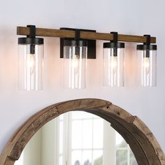 a bathroom light with three glass jars on the wall and a mirror in front of it