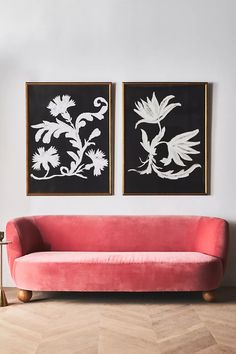 two black and white paintings hang on the wall above a pink couch in a living room