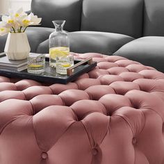 a coffee table with a tray on top of it next to a gray couch and white flowers