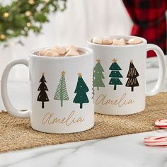 two coffee mugs with marshmallows in them sitting on a place mat