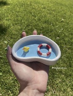 a hand holding a small bowl with a rubber duck in it and a life preserver