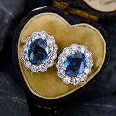 This flattering pair of earrings each feature one (1) oval cut natural sapphire set into a four-prong setting. The sapphires are each bordered with twelve (12) semi-bezel/ bead set round brilliant cut diamond accents. The diamonds are bordered with milgrain edging. The earrings measure 12.4mm by 10.5mm and are finished with friction backs. Luxury Oval Diamond Earrings For Anniversary, Luxury Hallmarked Oval Diamond Earrings, Timeless Oval Wedding Earrings, Luxury Oval Sapphire Diamond Earrings, Luxury Oval Diamond Earrings With Gemstones, Exquisite Oval Diamond Earrings For Anniversary, Classic Oval Sapphire Diamond Earrings, Sapphire Color Oval Diamond Earrings, Classic Blue Oval Diamond Earrings