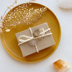 a yellow plate topped with a wrapped present next to a small crystal vase filled with flowers