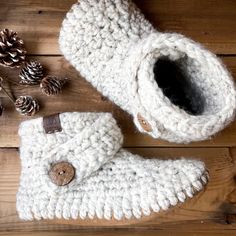 a pair of white crocheted boots sitting on top of a wooden floor next to pine cones