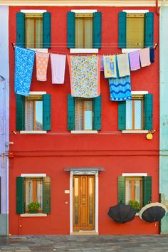 an orange building with green shutters and clothes hanging from it's front windows