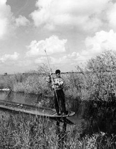 a man standing on top of a boat holding a fishing pole in his hand while he stands next to the water