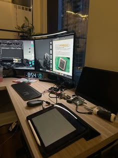 two computer monitors sitting on top of a desk next to a laptop and tablet pc