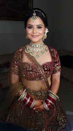 a woman in a red and gold bridal outfit with jewelry on her head, smiling at the camera