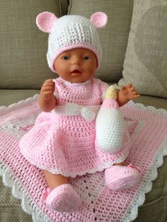 a baby doll sitting on top of a couch wearing a knitted pink outfit and hat