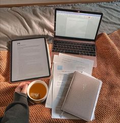 two laptops are sitting on a bed next to papers and a cup of tea