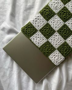 a green and white crocheted laptop cover sitting on top of a bed covered in sheets