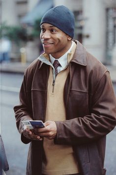 a man standing on the street holding a cell phone in his right hand and smiling