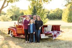 a family poses in front of an old red truck