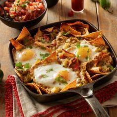 a pan filled with eggs and nachos on top of a table next to salsa