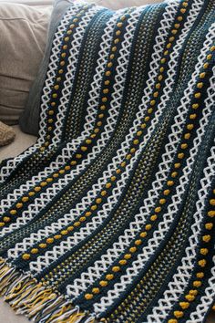 a crocheted blanket sitting on top of a couch next to a pillow and pillows