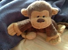 a stuffed monkey laying on top of a bed next to a blue and white blanket