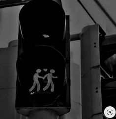 a black and white photo of a traffic light with two people walking on the crosswalk