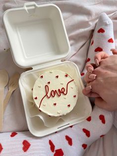 a cake with the word love written on it is in a plastic container next to a spoon and utensils