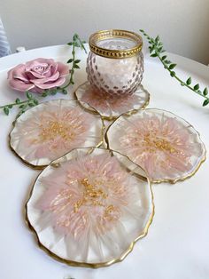 four pink flowers are sitting on a white table with a candle and some greenery