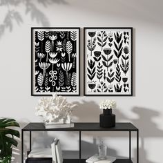 two black and white art prints hanging on the wall next to a table with flowers