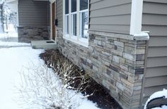 a house with snow on the ground next to it and bushes in front of the house