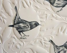 two birds sitting on top of a white plate covered in black and white paper with leaves