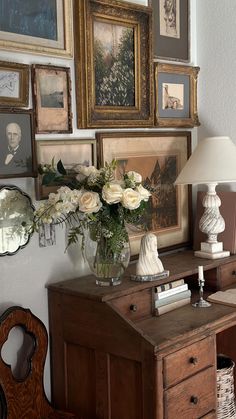 a desk with flowers and pictures on the wall above it, along with a lamp