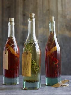 three wine bottles filled with different types of liquid and herbs on top of a table