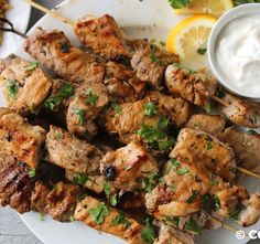 chicken skewers on a plate with lemon wedges and sour cream