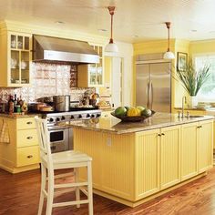 a kitchen with yellow cabinets and an island that has fruit on top of it in front of the stove