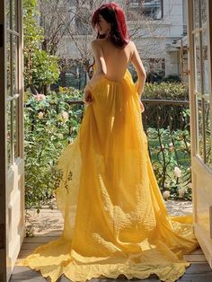 a woman in a yellow dress is looking out an open door at the garden outside