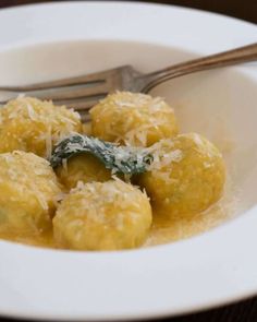 a white bowl filled with meatballs covered in grated cheese next to a fork