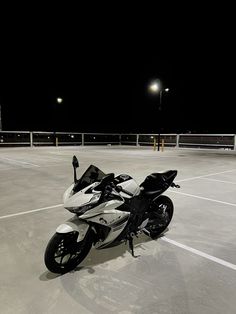 a motorcycle is parked in an empty parking lot at night with its lights turned on