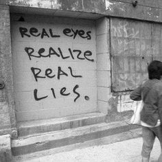 two people walking down the street in front of a building with graffiti written on it